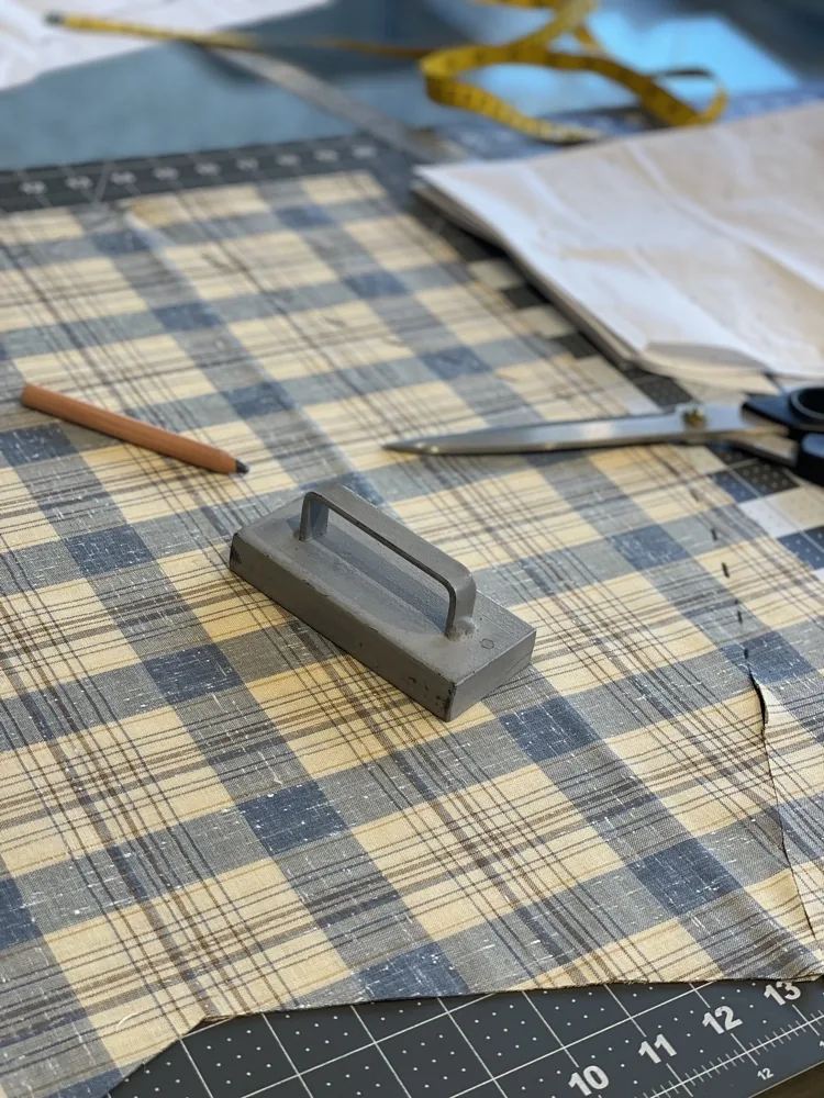 Tailor's tools on the cutting table — chalk weight, shears, and pencil on plaid fabric